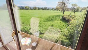 A room with a large window overlooking a green field with trees and a clear sky. - Stoneycross Cottage (Preston)