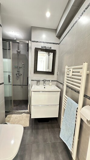 A modern bathroom with a glass-enclosed shower, a white vanity with a mirror, and a towel rack.