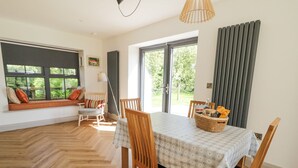 A dining area with a table set for four, wooden chairs, a woven basket with items, and a view through a glass door to the outdoors. - Corradillar Quay Cottage (Enniskillen)