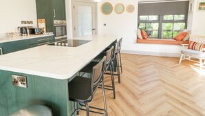 A modern kitchen with a large island, bar stools, and a seating area by a window. - Corradillar Quay Cottage (Enniskillen)