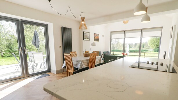 A modern kitchen with a large island, sliding glass doors leading to a patio, and a dining area with a table and chairs. - Corradillar Quay Cottage (Enniskillen)