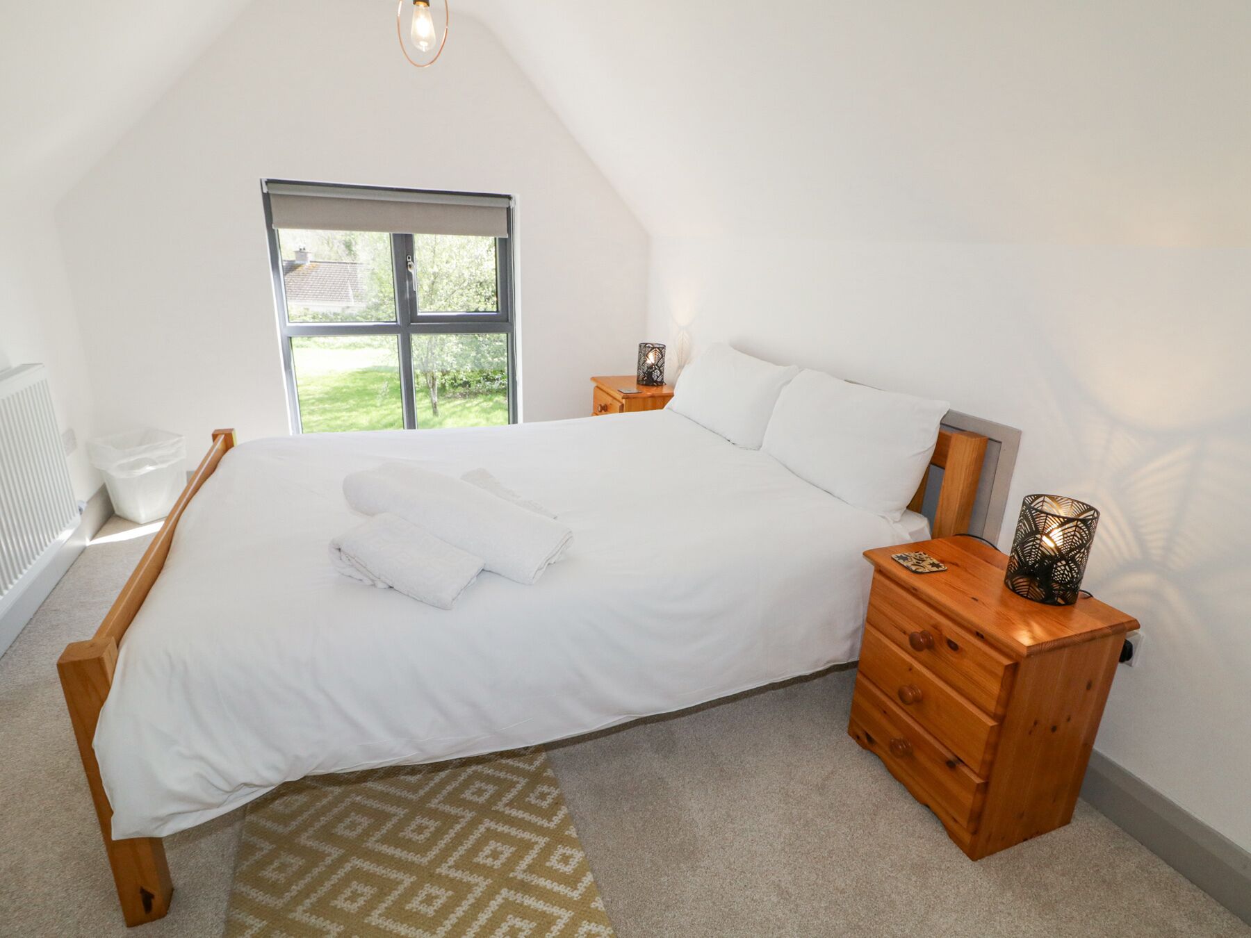 A bedroom with a large bed, wooden nightstands, a window with a view, and a radiator.