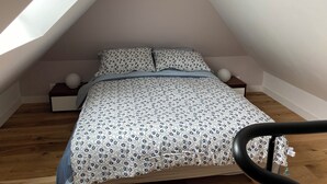 Une chambre avec un plafond en pente, un lit recouvert d’une literie à motifs, deux tables de chevet surmontées de lampes sphériques et un plancher en bois.