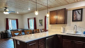 A modern kitchen with wooden cabinets, a marble countertop, and a built-in dishwasher. - Dolly Varden Cabin - Modern Vacation Home in Cooper Landing (Cooper Landing)