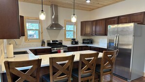 A modern kitchen with wooden cabinets, a stainless steel refrigerator, a gas stove, and a large island with bar stools.
