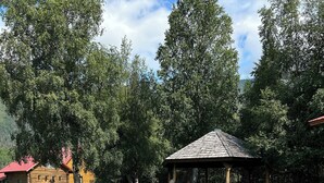 A wooden cabin with a red roof, a gazebo, and a gravel path.