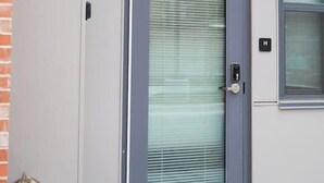 A modern building with a grey door, a small window, and a metal doorbell.