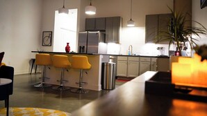 A modern kitchen with bar stools, stainless steel appliances, and pendant lighting.