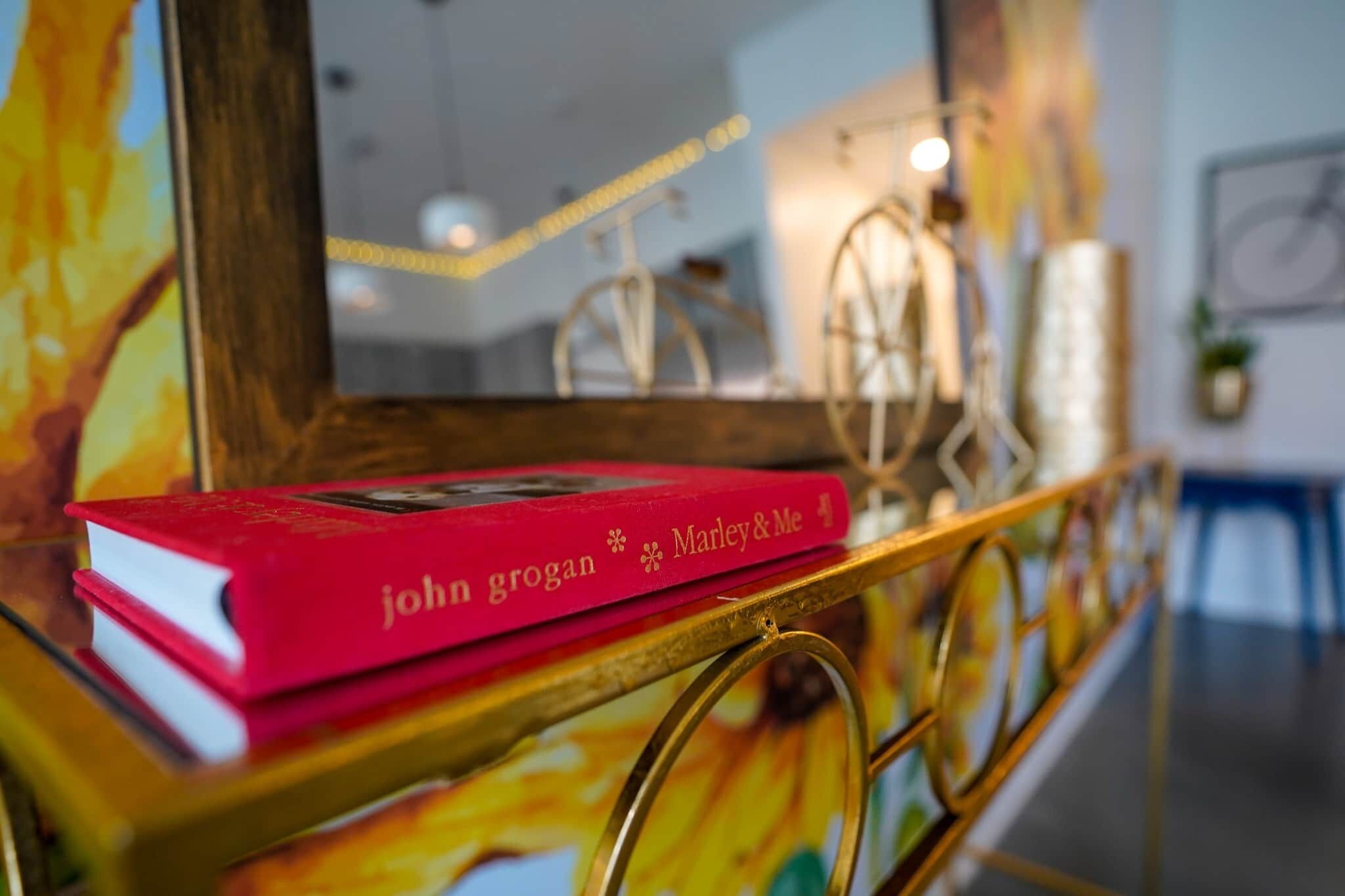 Een rood boek met de titel 'John Grogan Marley & Me' op een plank met een gouden lijst.