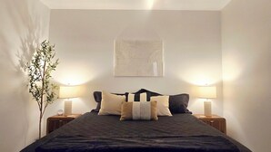 Een slaapkamer met een bed, twee nachtkastjes met lampen, een plafondventilator, een aan de muur hangend kunstwerk en een plant.