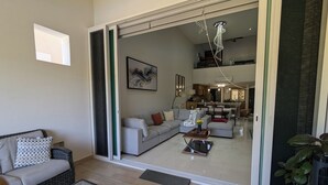 A modern living room with a sofa, coffee table, and a dining area visible through a glass door.