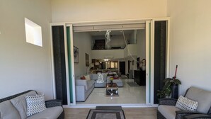 A spacious living area with a sofa set, a coffee table, and a dining area visible through an open sliding door.