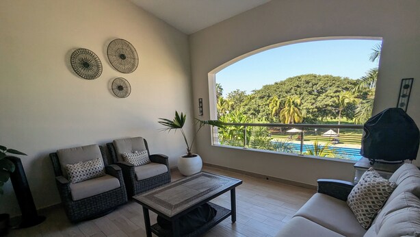 A living room with a sofa, two armchairs, a coffee table, and a large window with a view of a pool and greenery.