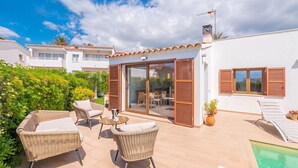 Una villa moderna con piscina, mobiliario exterior y puerta de cristal que da a un patio.