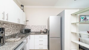 A compact kitchen with white cabinets, a microwave, a kettle, and a stainless steel refrigerator. - CapeCity Studio~ Walk 5mins>V&A Waterfront & CTICC (Cape Town)