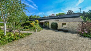 A stone building with a gravel driveway, surrounded by greenery and trees. - Eco 2-Bed Bungalow with Biodiverse Garden & Solar (Bestwood Village)