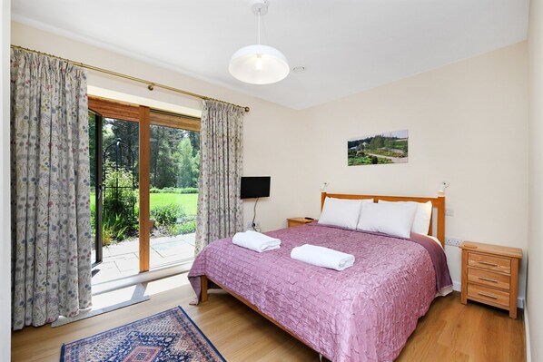 A bedroom with a bed, a bedside table, a nightstand, a TV, and a window with curtains.