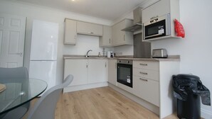A compact kitchen with white cabinets, a microwave, an oven, and a trash bin. - NEW Immaculate Garden Flat (Cliftonville)