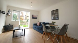 A modern living room with a glass dining table, grey chairs, a blue sofa, and a black coffee table. - NEW Immaculate Garden Flat (Cliftonville)