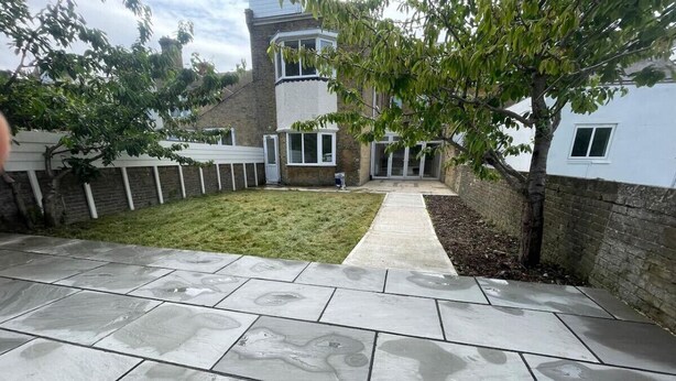 A paved patio with a grassy area and a pathway leading to a building with a white facade and multiple windows. - NEW Immaculate Garden Flat (Cliftonville)