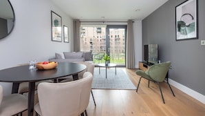 A modern living room with a round dining table, grey sofa, and a TV on a stand.