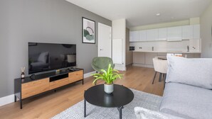 A modern living room with a flat-screen TV, a grey sofa, a black coffee table, and a green chair.