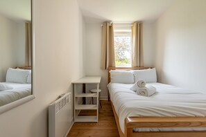Ein kleines, sauberes Zimmer mit einem Bett, einem Schreibtisch und einem Fenster mit Vorhängen.