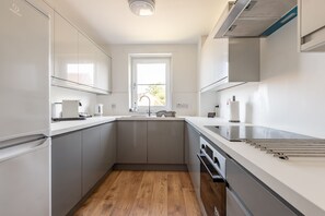 Eine moderne Küche mit grauen Schränken, Holzboden, einem Fenster und einer Edelstahl-Dunstabzugshaube.