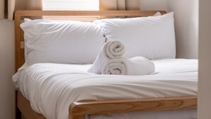 A neatly made bed with white linens and pillows, a wooden headboard, and a window with curtains. - Kate Kennedy Court (No 2) (St Andrews)