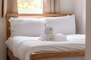 A neatly made bed with white linens and pillows, a wooden headboard, and a window with curtains. - Kate Kennedy Court (No 2) (St Andrews)