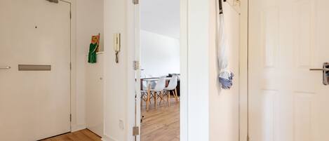 A hallway with wooden flooring, white doors, and a dining area visible through an open door.