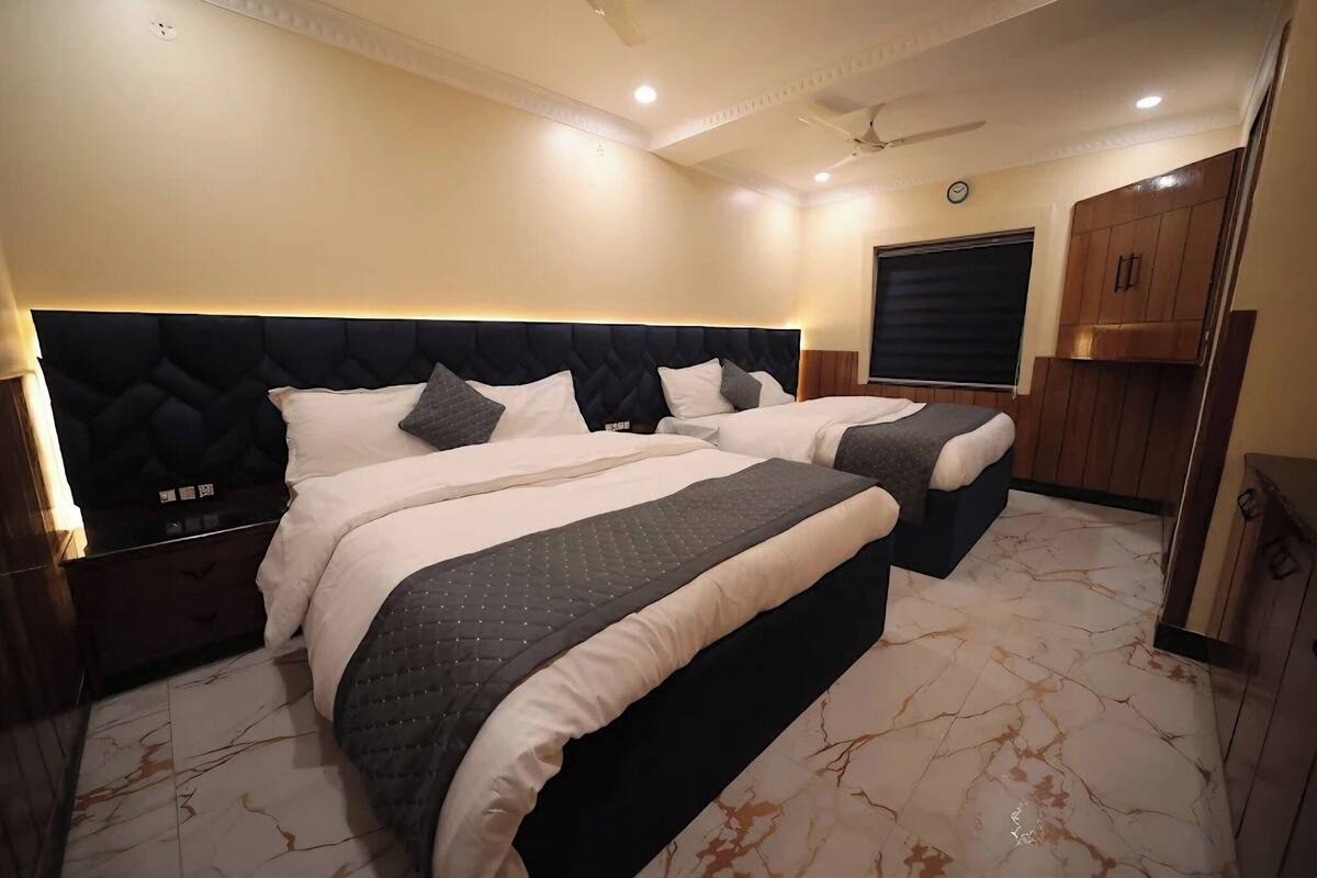 Quarto de hotel com duas camas, cabeceira escura, guarda-roupa de madeira e piso de mármore.