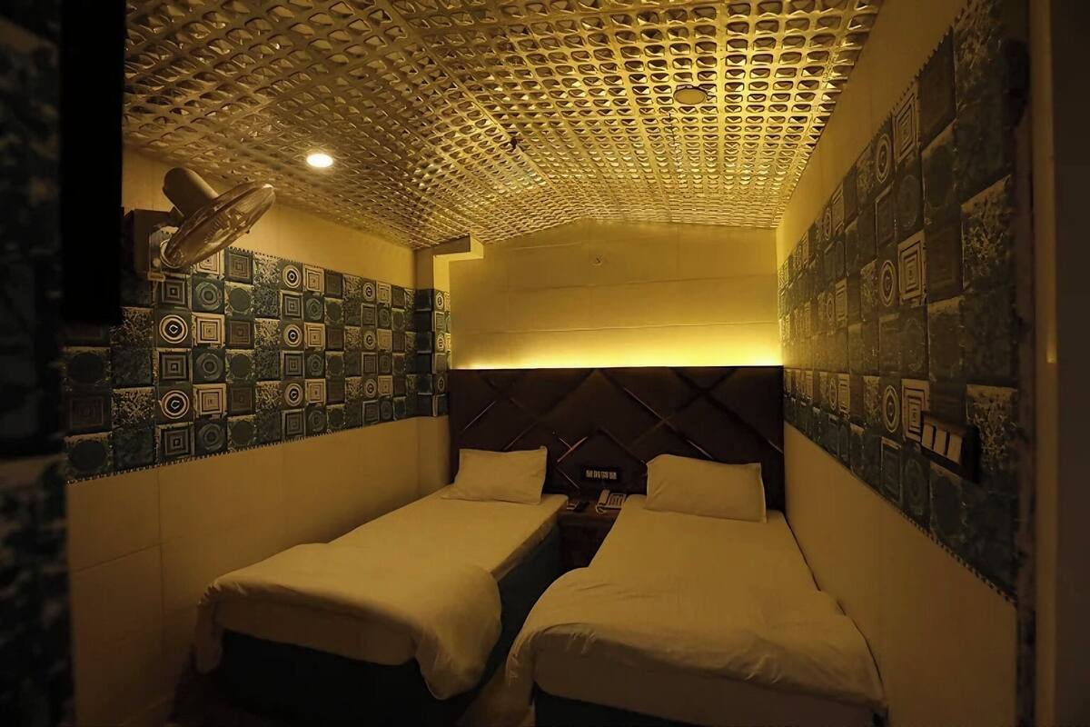 Quarto com duas camas, parede estampada, ventilador de teto e luminária.