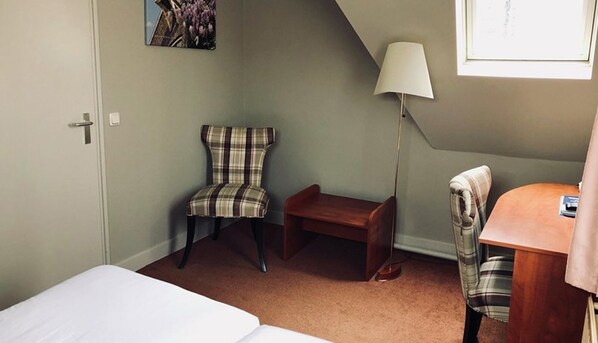 Cozy retreat with a bed, bench, chair, and floor lamp, featuring a sloped ceiling and a window.