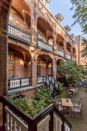 Experience the charm of this classic building with its arched windows and balcony railing, surrounded by lush greenery and a tranquil courtyard.