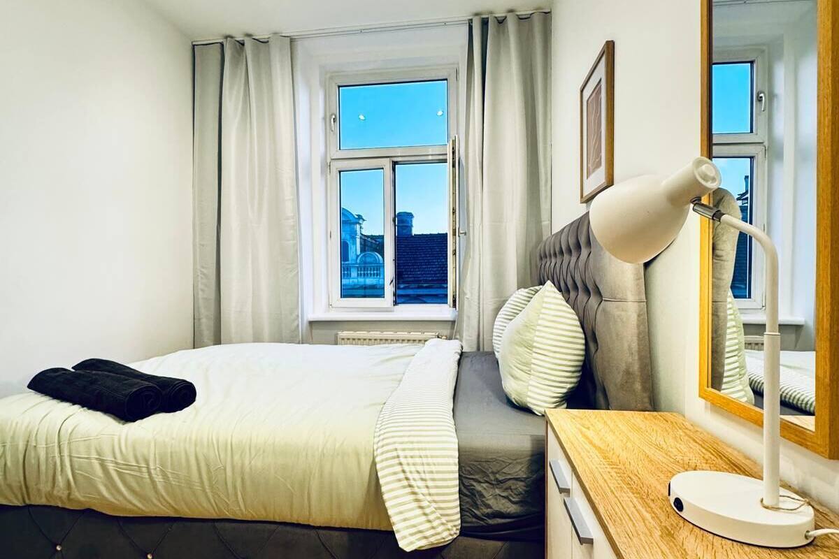 A modern bedroom with a bed, a desk, a lamp, and a large window.