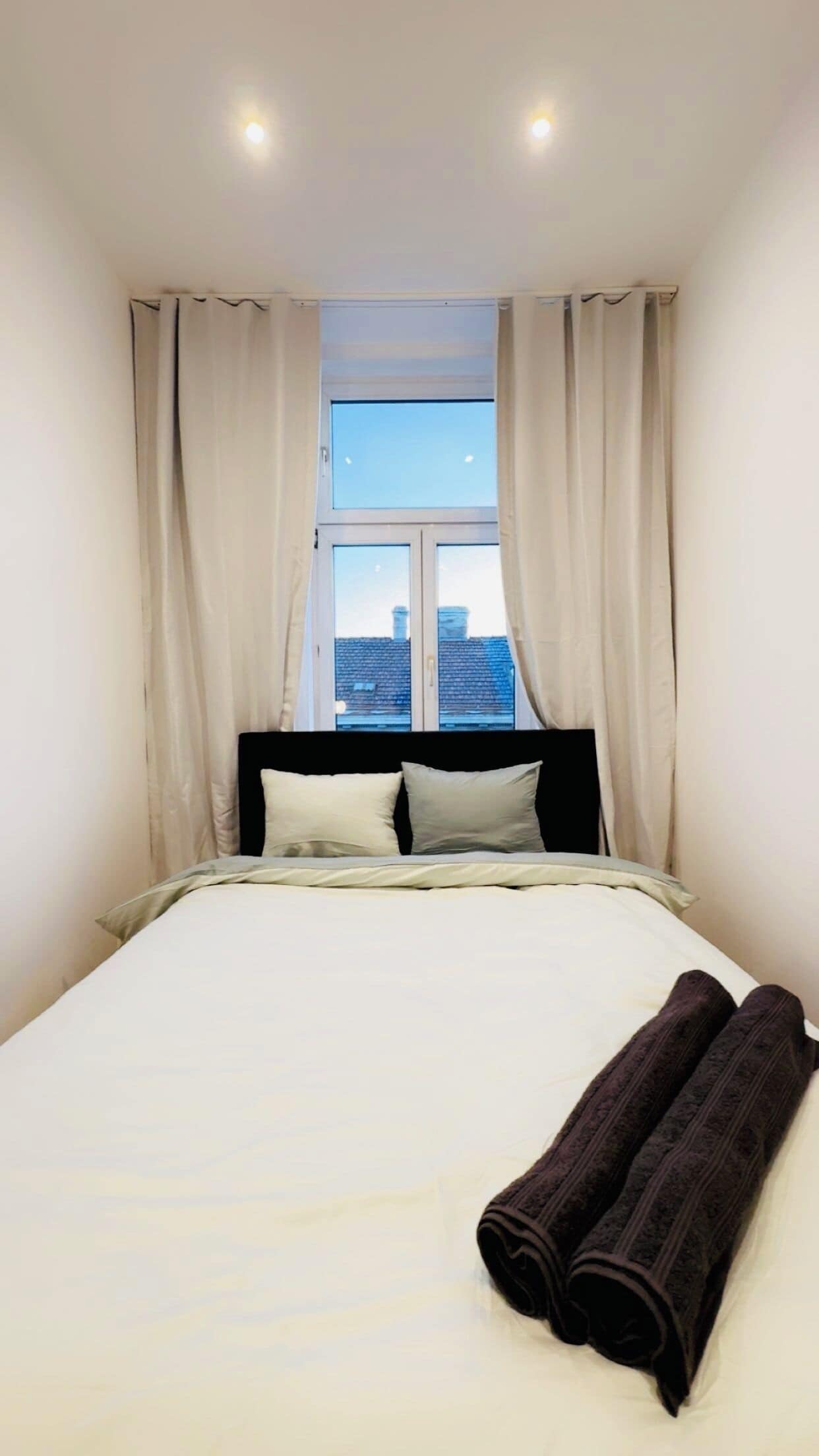 Ein Hotelzimmer mit Bett, einem Fenster mit Vorhängen und Blick auf die Stadtlandschaft.