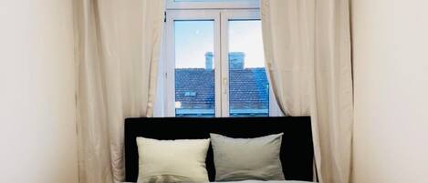 Ein Hotelzimmer mit Bett, einem Fenster mit Vorhängen und Blick auf die Stadtlandschaft.