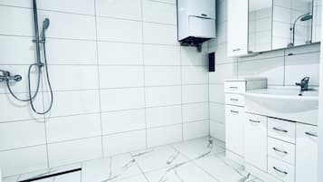 A modern bathroom with white tiles, a marble floor, a shower, a sink, and a mirror.