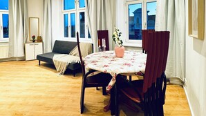 Una habitación amplia con suelo de madera, una mesa de comedor con sillas, un sofá y un ventanal con cortinas.