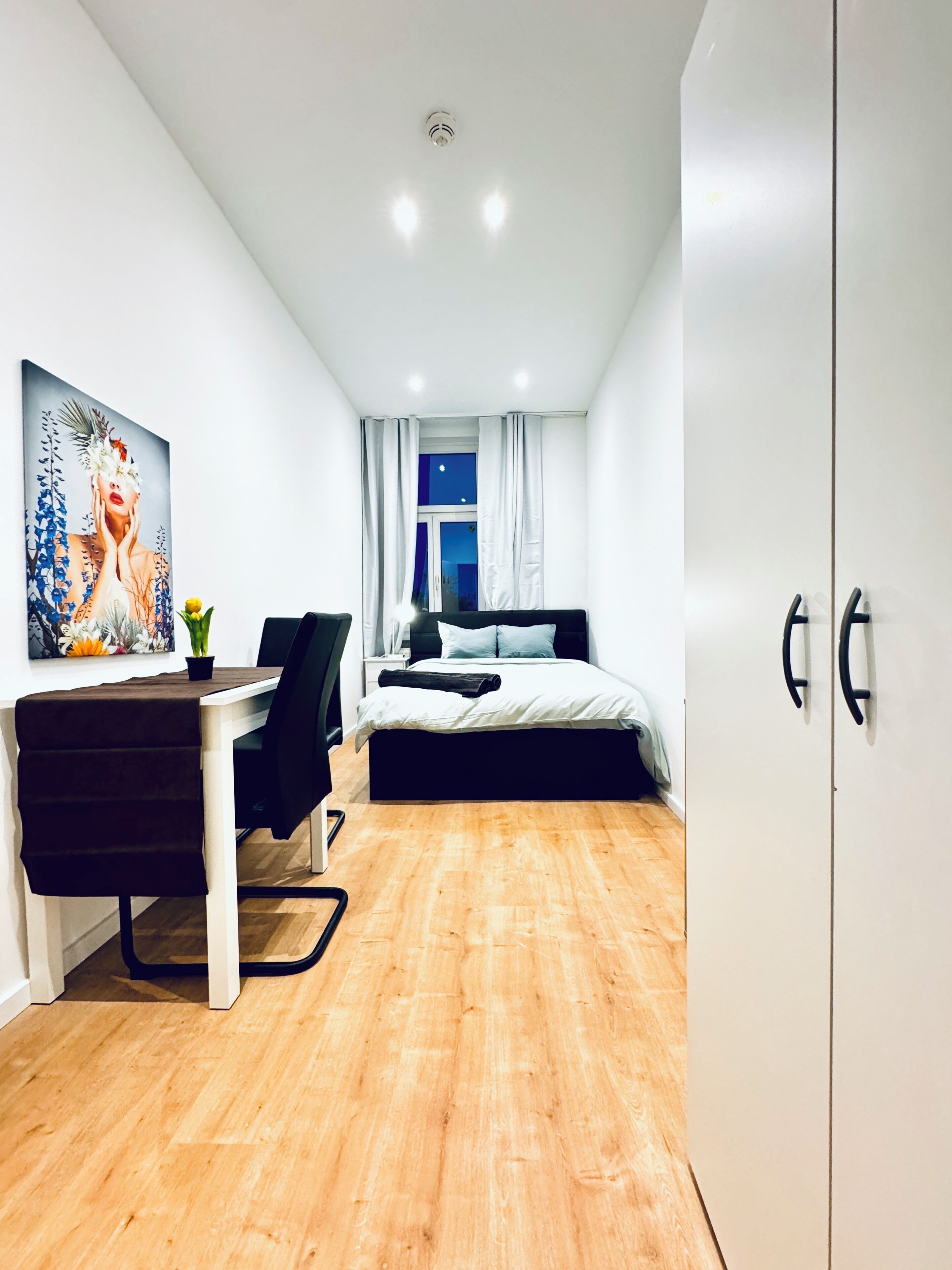 Un dormitorio moderno con una cama, un escritorio y una silla. Hay un cuadro en la pared y una ventana con cortinas.