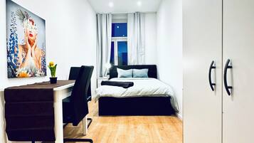 Un dormitorio moderno con una cama, un escritorio y una silla. Hay un cuadro en la pared y una ventana con cortinas.