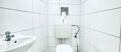 Un baño con azulejos blancos, suelo de mármol, lavamanos, inodoro y bidé.