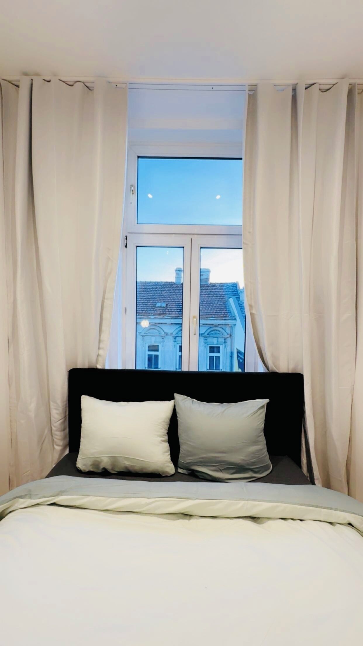 A bedroom with a bed, two pillows, and a window with curtains.