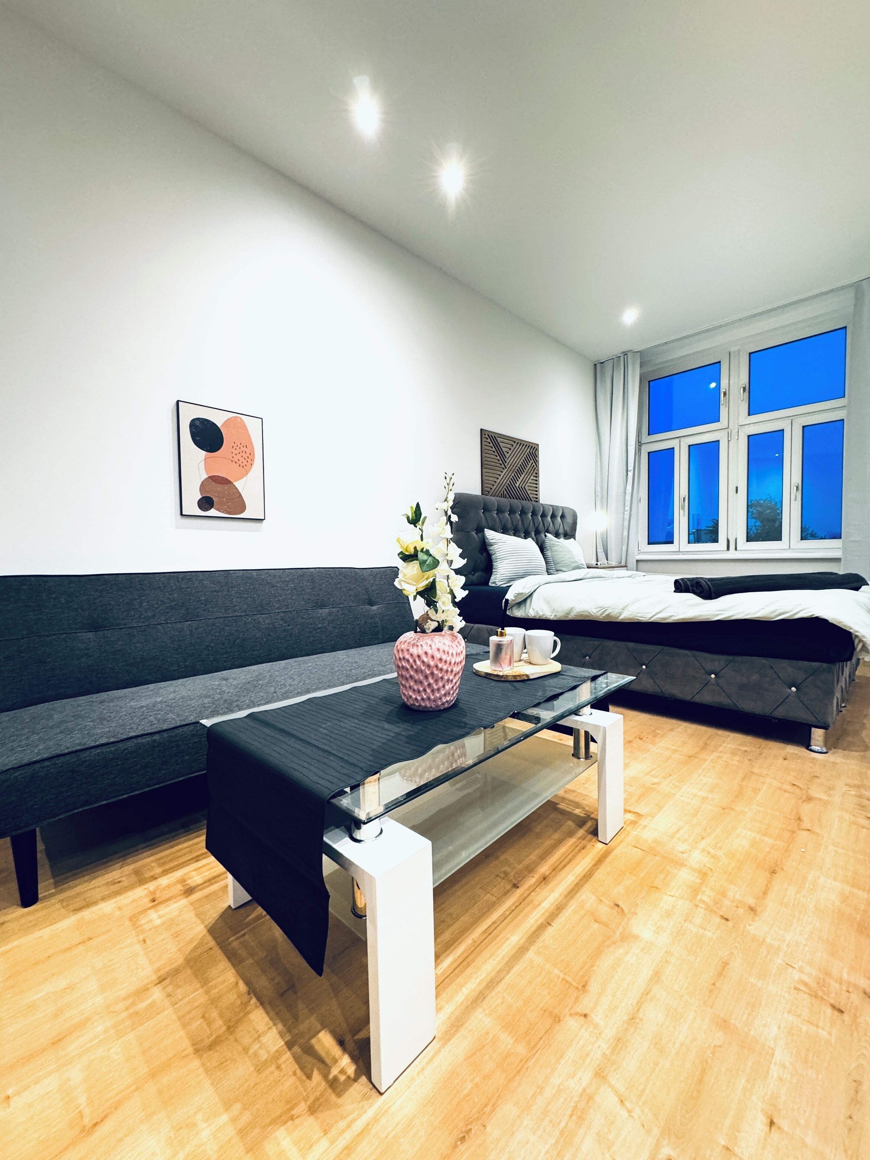 En moderne stue med sofa, sofabord i glas og en seng.