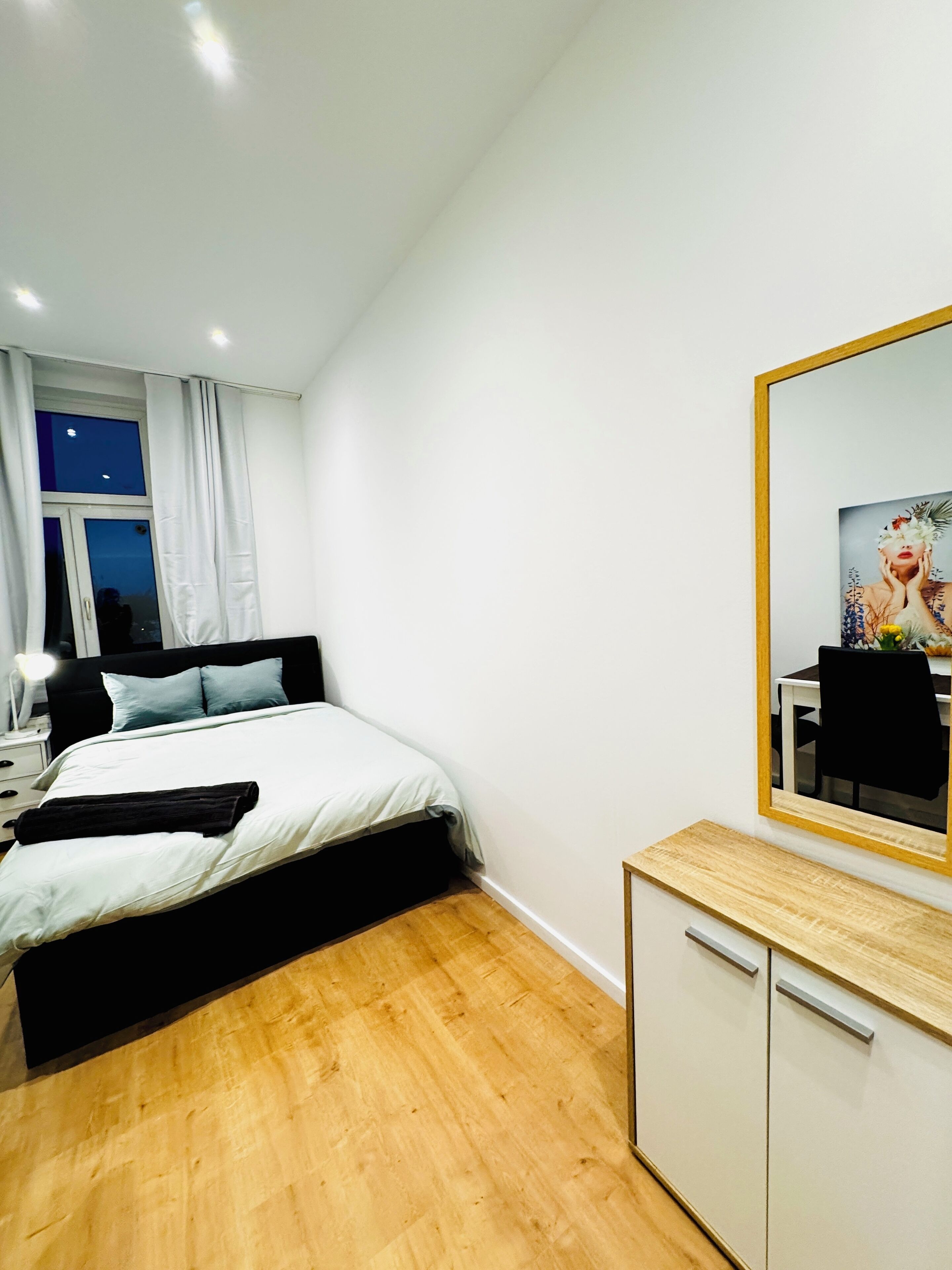 Un dormitorio moderno con cama, mesita de noche y un espejo grande.