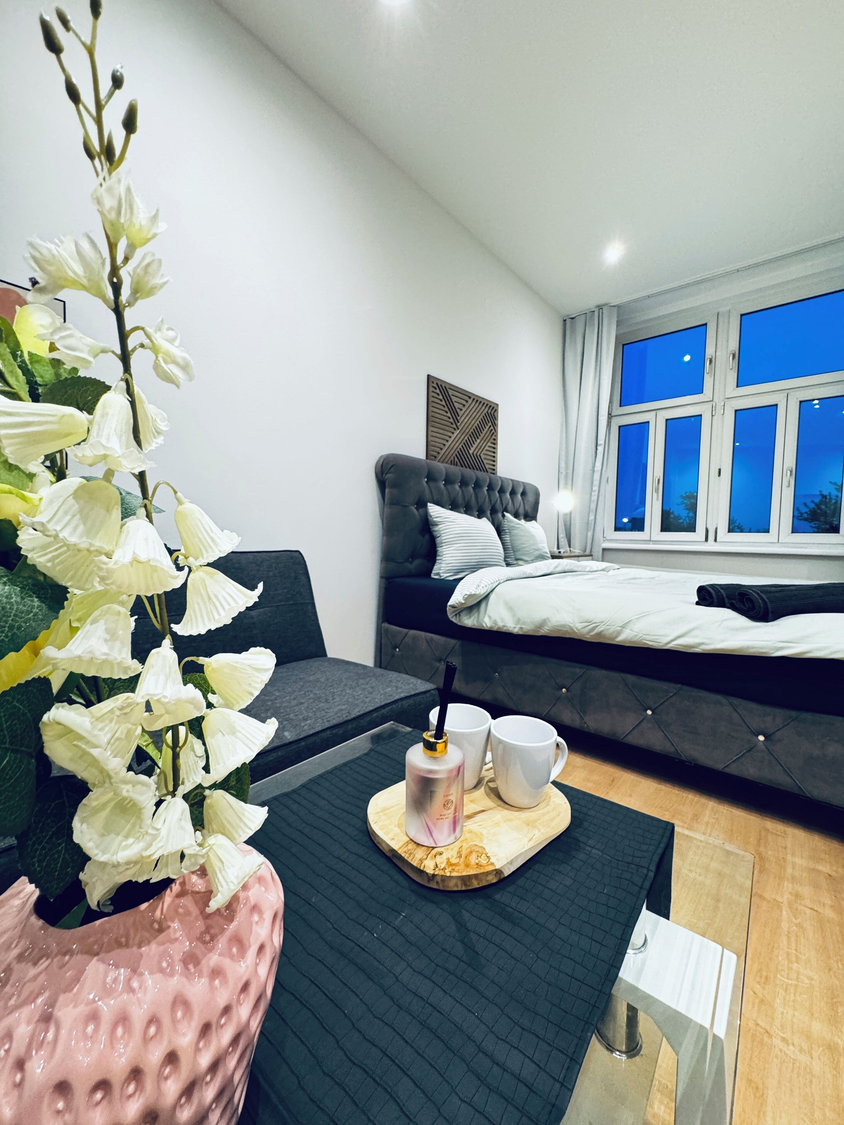 Ein modernes Schlafzimmer mit Bett, Nachttisch, Blumentopf und Fenster mit Blick.