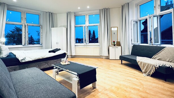 Una sala de estar moderna con sofá, cama, una mesita y ventanas amplias que ofrecen vistas al exterior.