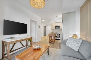 A modern living room with a flat-screen TV, wooden coffee table, grey sofa, and a kitchen in the background. - Bright & Modern Downtown Stay (Kitchener)