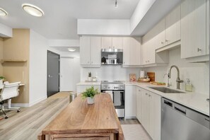A modern kitchen with white cabinetry, a wooden dining table, and a built-in oven. - Bright & Modern Downtown Stay (Kitchener)